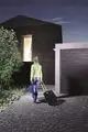 Eine Frau mit Gepäck vor einem modernen Haus mit Theben Präsenzmelder.